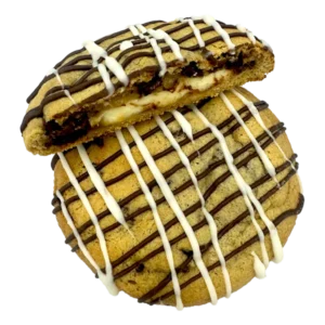 A creamy cheesecake filling stuffed inside a giant chocolate chip cookie, drizzled with white and milk chocolate