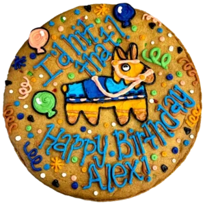 Giant chocolate chip cookie cake, decorated in a bright fiesta theme with a frosted piñata and text that reads "I'd hit that, happy birthday Alex".
