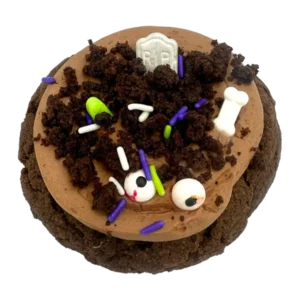 Giant chocolate graveyard cookie topped with chocolate mousse, brownie crumbs, candy bones, candy eyes, and a tombstone decoration for Halloween.