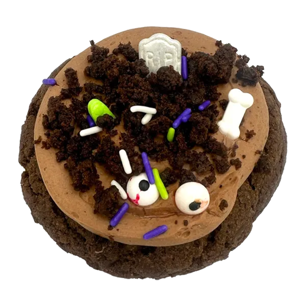 Giant chocolate graveyard cookie topped with chocolate mousse, brownie crumbs, candy bones, candy eyes, and a tombstone decoration for Halloween.