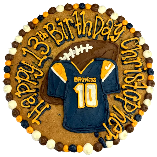 Giant chocolate chip cookie cake, decorated in a football theme with a frosted jersey and football and happy birthday text.
