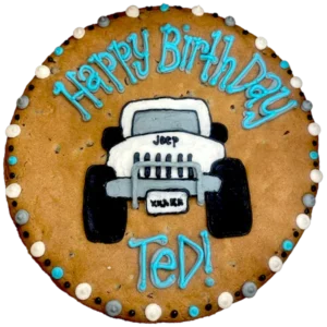 Giant chocolate chip flavored cookie cake decorated with a frosted 4x4 Jeep and text that reads "happy birthday Ted".