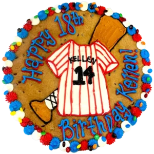 Giant chocolate chip cookie cake decorated in a baseball theme with a frosted baseball jersey and bat and text that reads "happy birthday Kellen".