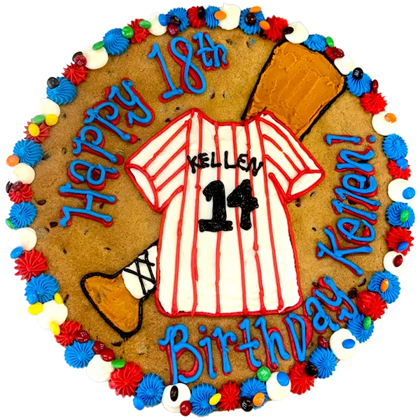 Giant chocolate chip cookie cake decorated in a baseball theme with a frosted baseball jersey and bat and text that reads "happy birthday Kellen".