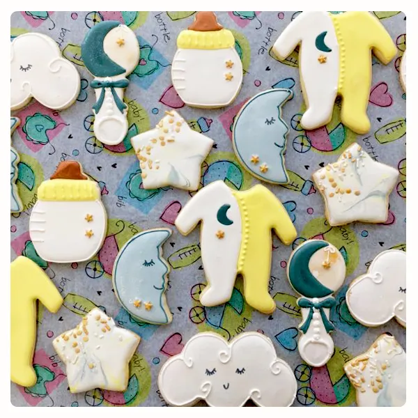 Hand decorated baby shower sugar cookies featuring baby bottles, onesies, moons, stars, rattles, and clouds