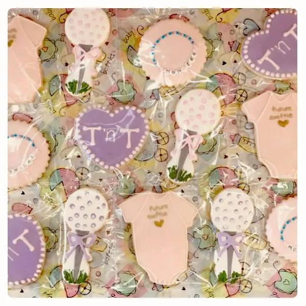 Personalized baby shower sugar cookies with balloons, hearts, baby onesies, and custom names in pink and lavender