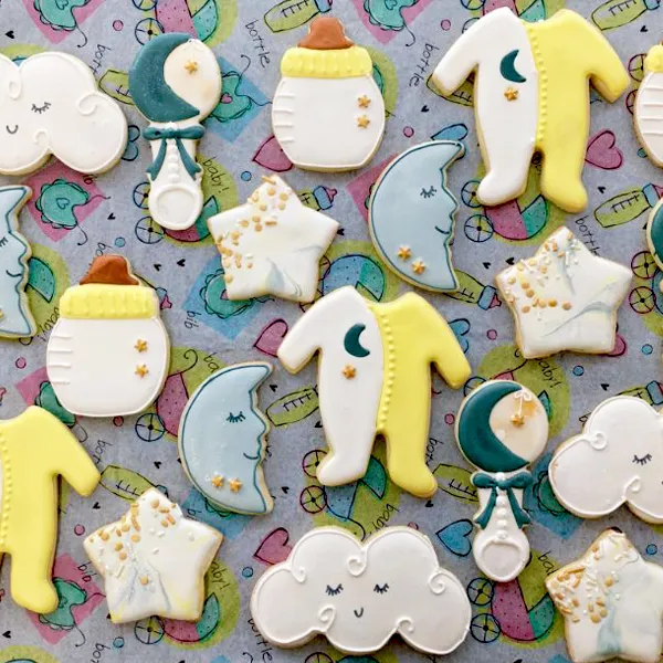Hand decorated baby shower sugar cookies featuring baby bottles, onesies, moons, stars, rattles, and clouds