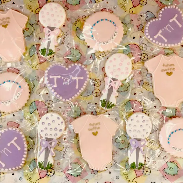 Personalized baby shower sugar cookies with balloons, hearts, baby onesies, and custom names in pink and lavender