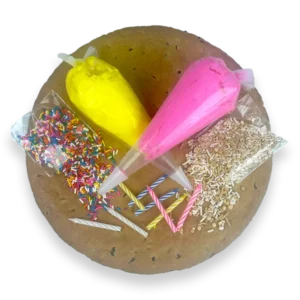 Cookie Cake Decorating Kit with a 12-inch diameter plain round chocolate chip cookie cake, 2-icing bags, 2-bags of sprinkles, and colorful candles for decorating at home.