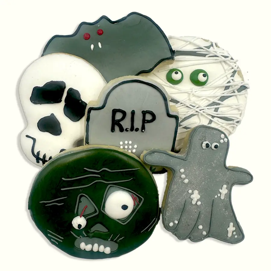 Assortment of decorated Halloween sugar cookies featuring a skull, mummy, bat, tombstone, ghost, and spooky green monster.